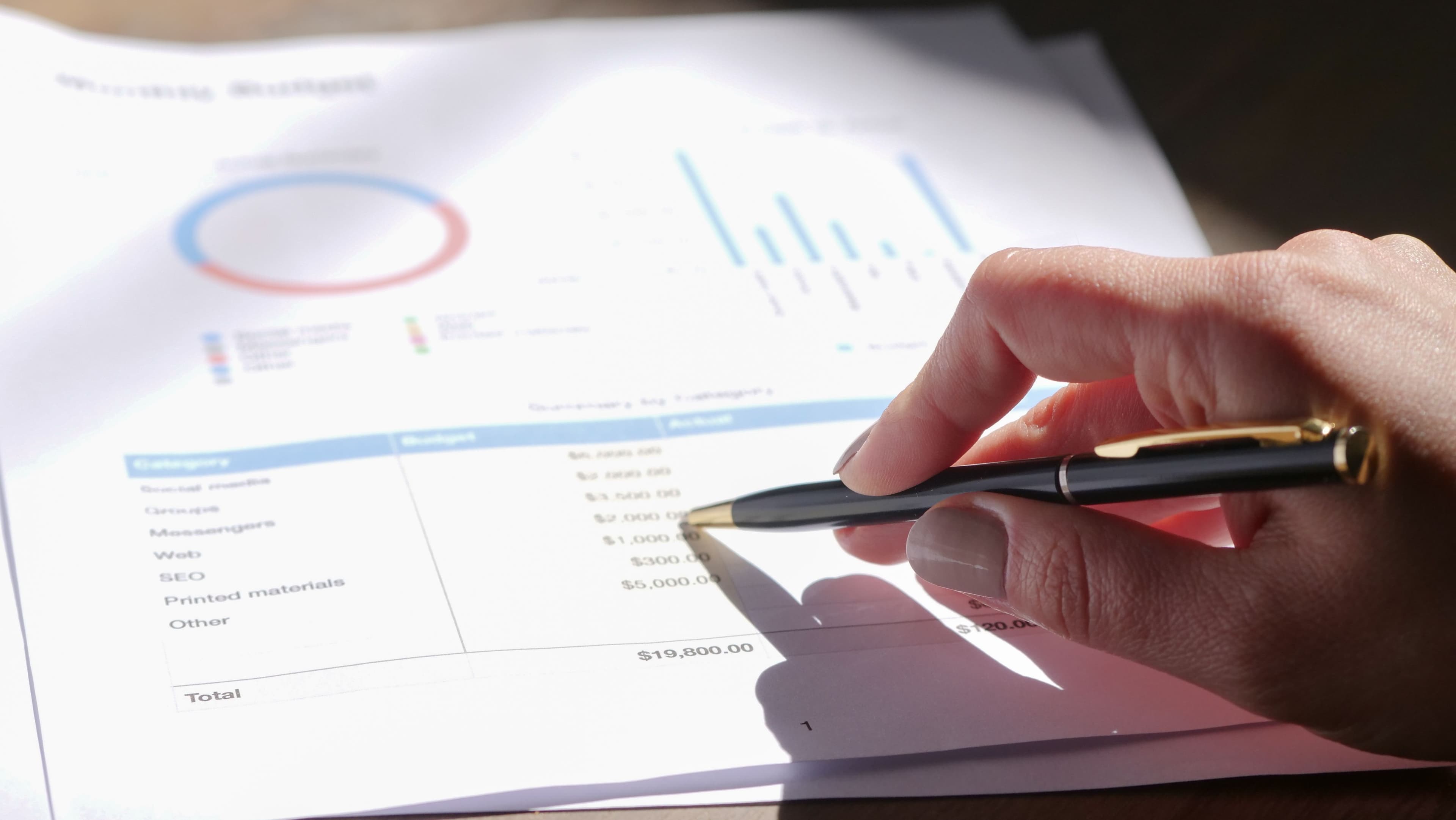 Hand reviewing a monthly budget report with charts and financial data