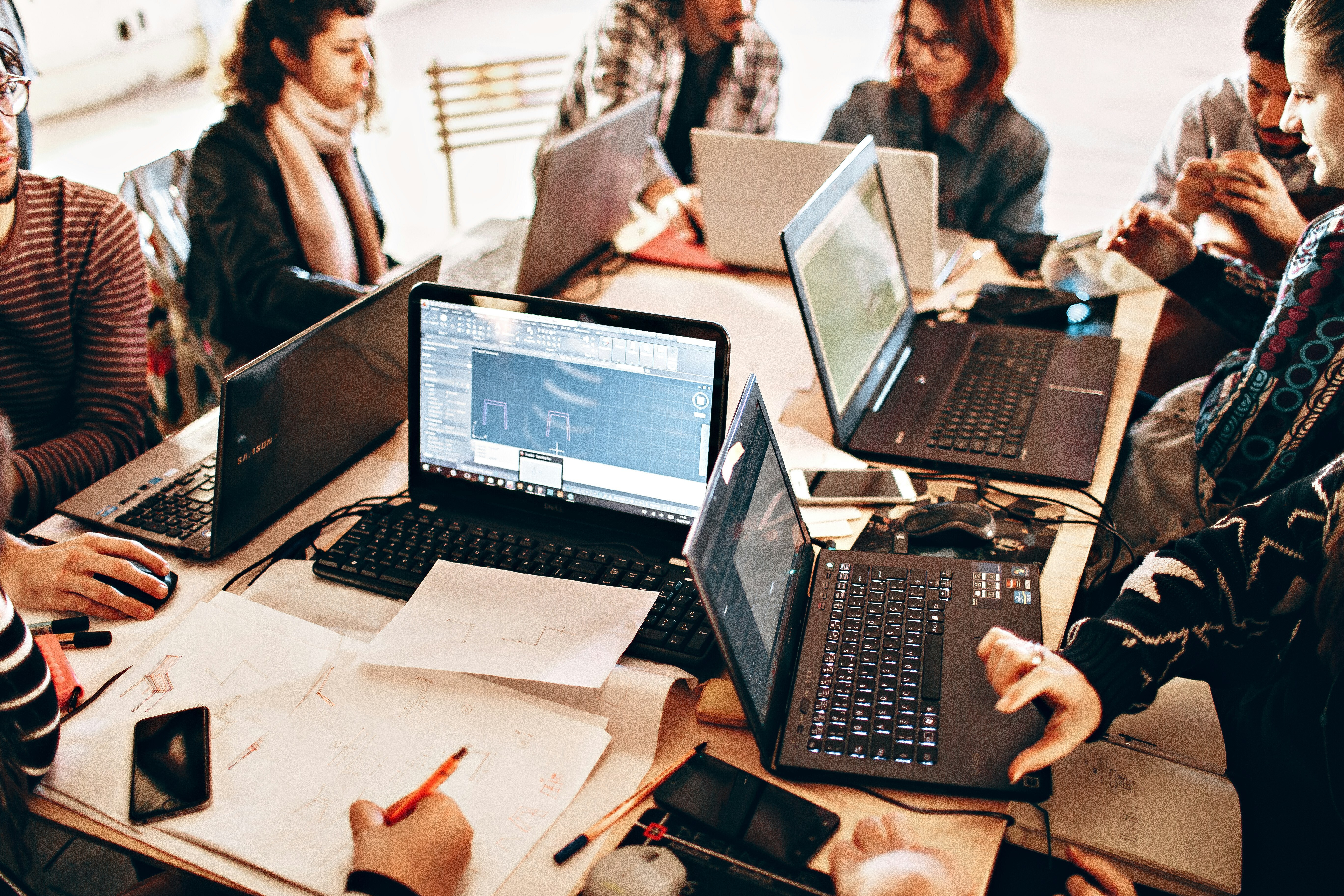 University students collaborating around laptops and design sketches